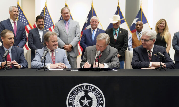 Texas Gov Greg Abbott signs Senate Bill 1, also known as the election integrity bill, into law with State Sen. Bryan Hughes ( R-Mineola), front center left, Andrew Murr (R-Junction),  front left, and Lieutenant Governor Dan Patrick, front right, looking on with others in the back ground in Tyler, Texas, on Sept. 7, 2021. (LM Otero/AP Photo)