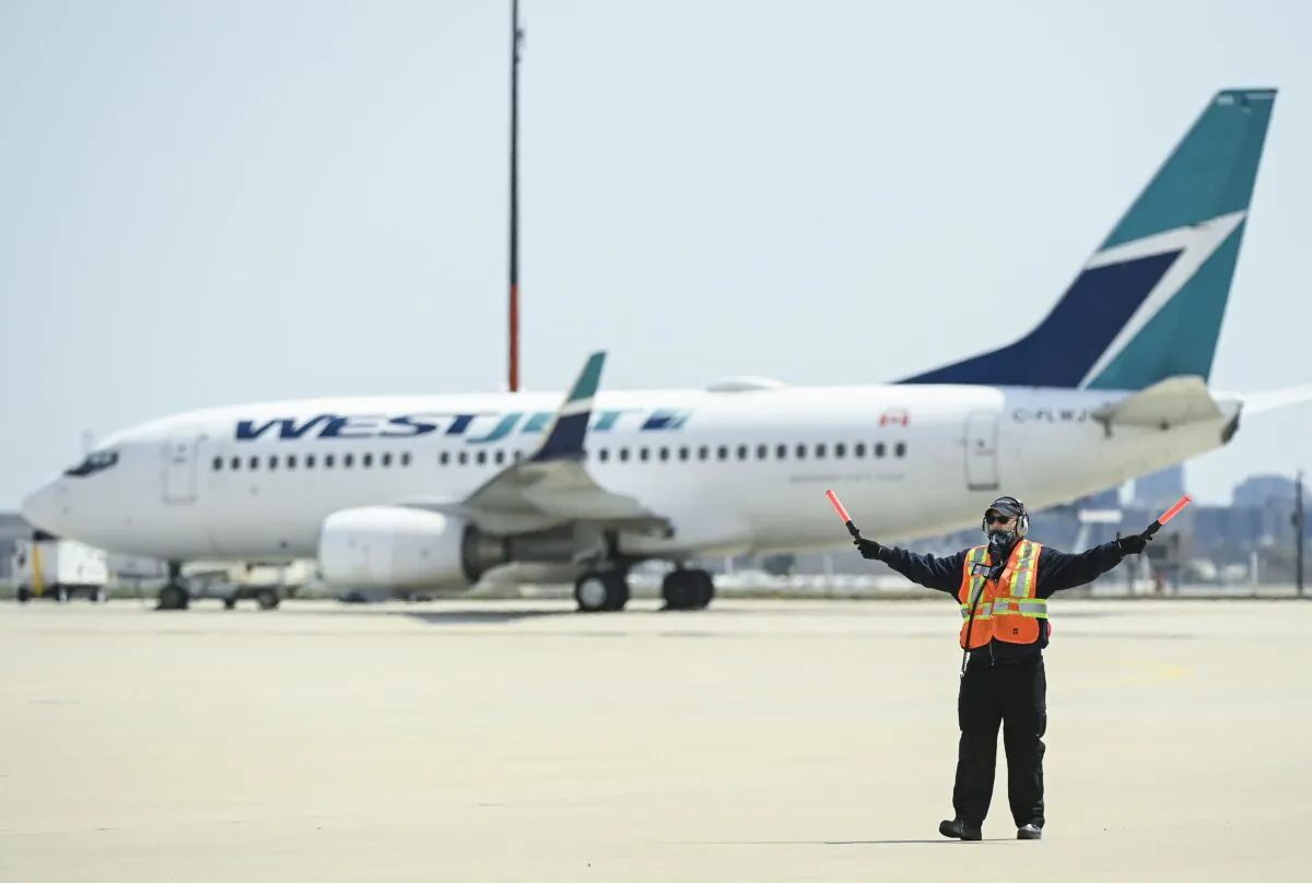 A ground controller works as a WestJet plane sits on the tarmac at Pearson International Airport in Toronto on April 27, 2021. (Nathan Denette/The Canadian Press)