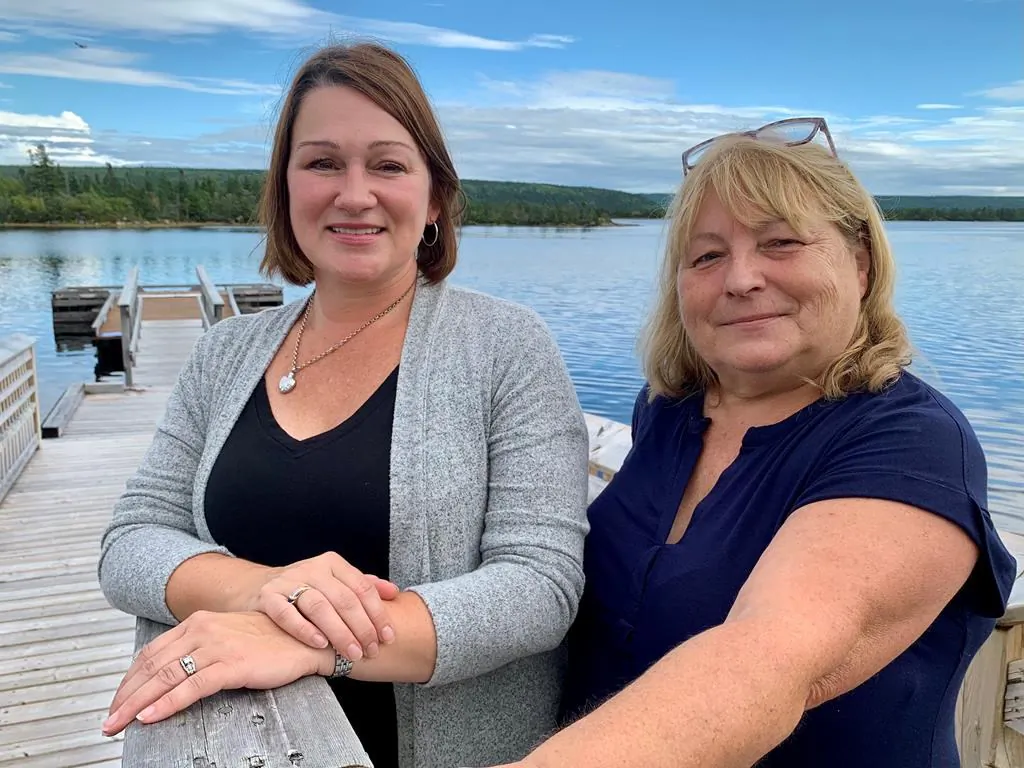 Barbara Pritchett, left, and Carol Anne Loveless, right, stand on a deck in front of the Gambo River in Gambo, N.L., on Sept. 3, 2021. They co-wrote a play documenting the massive efforts undertaken by the people of Gambo to look after hundreds of passengers whose planes were rerouted to the nearby town of Gander on Sept. 11, 2001. (The Canadian Press/Sarah Smellie)