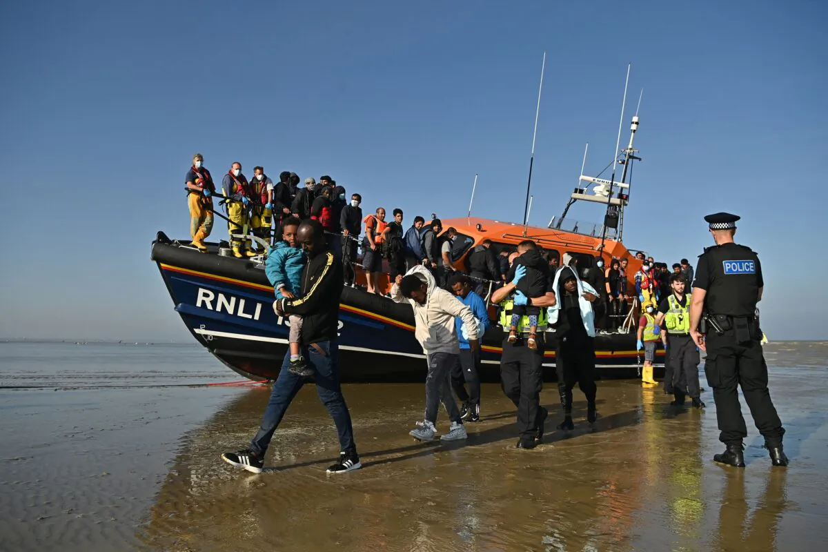 Illegal imigrants carry children as they are escorted to be processed after being picked up by an Royal National Lifeboat Institution lifeboat while crossing the English Channel at a beach in Dungeness, southeast England, on Sept. 7, 2021. (Ben Stansall/AFP via Getty Images)