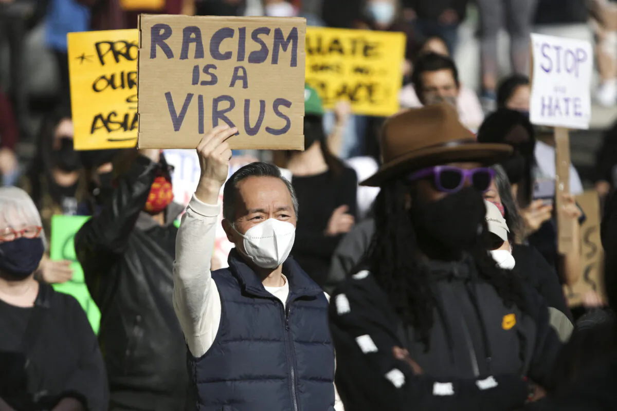 A man holds a sign that reads "Racism is a Virus" during the "We Are Not Silent" rally against anti-Asian hate in response to recent anti-Asian crime in the Chinatown-International District of Seattle, Washington on March 13, 2021. (Jason Redmond/AFP via Getty Images)