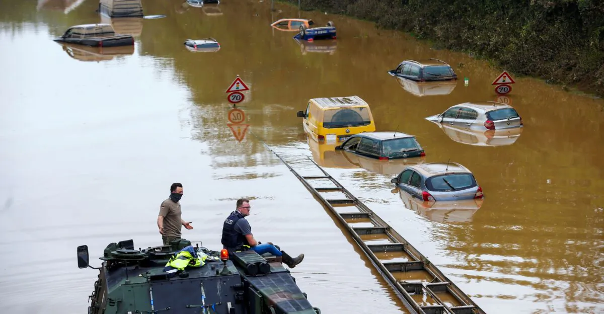 A police officer and a member of the Bundeswehr forces look at partially submerged cars on a flooded road following heavy rainfalls in Erftstadt-Blessem, Germany on July 17, 2021. (Thilo Schmuelgen/Reuters)