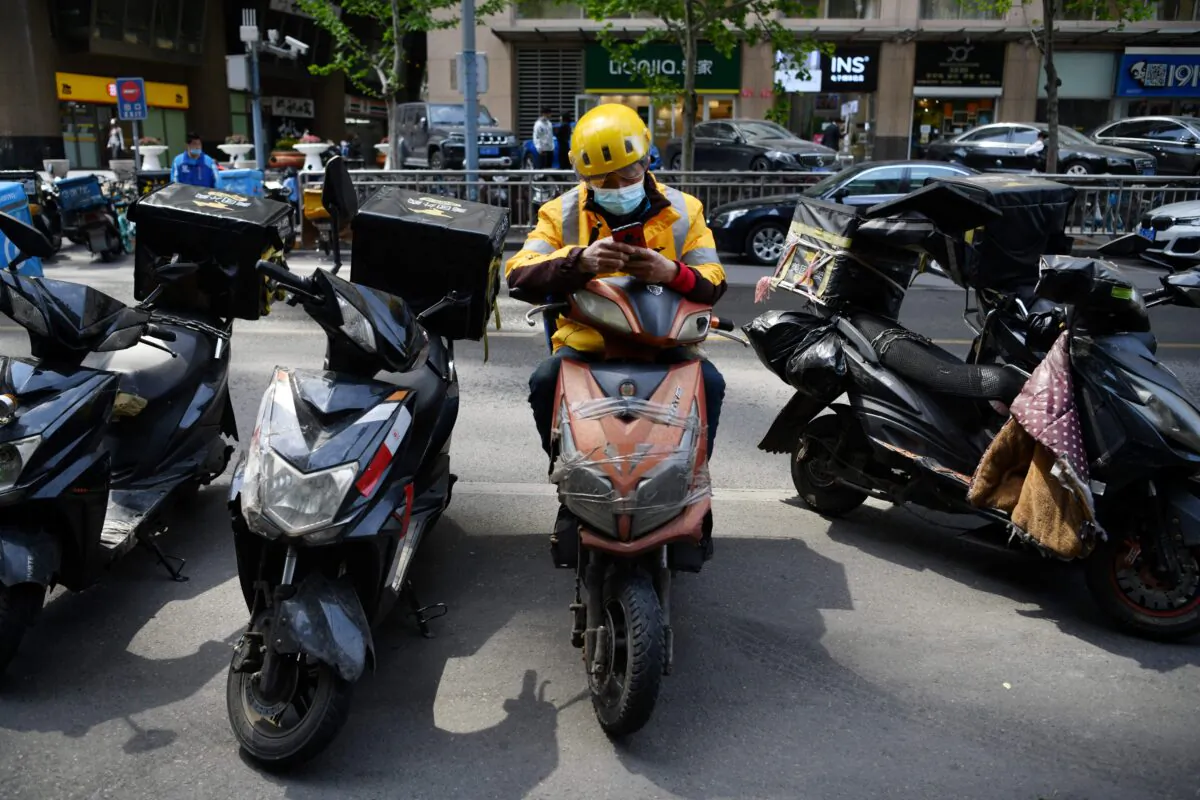 A delivery rider for Meituan, one of China's biggest food delivery firms, waits for orders outside a restaurant in Beijing on April 27, 2021. (Greg Baker/AFP) 