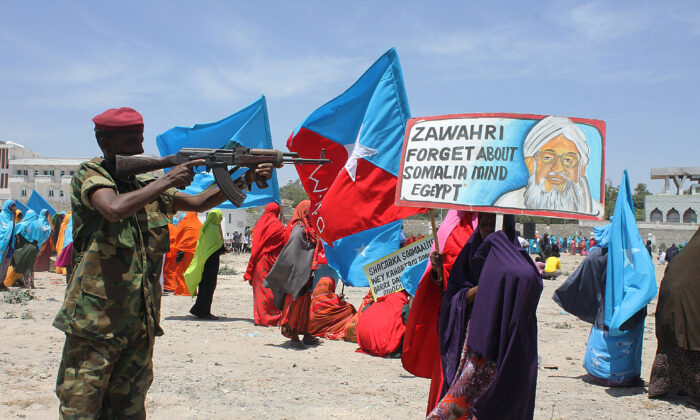 2014 年 2 月 23 日，在摩加迪沙举行的反青年党集会期间，一名索马里安全士兵用步枪指着一张海报，上面有基地组织领导人艾曼·扎瓦希里 (Ayman al-Zawahiri) 的照片。（Abdifitah Hashi Nor/AFP via Getty Images）
