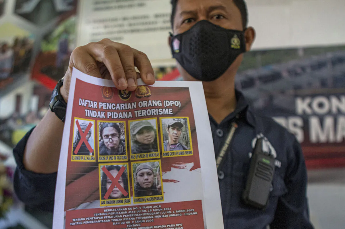 A police officer shows a wanted poster displaying, among others, portraits of two terrorists Ali Kalora (top L) and Jaka Ramadan (bottom L), who were killed during shootout with security forces, during press conference at the Parigi Moutong Police Station, Central Sulawesi, Indonesia, on Sept. 19, 2021. (Mohammad Taufan/AP Photo)