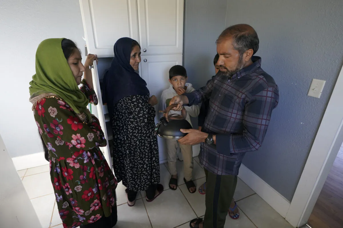 Abdul, right, who worked as a mechanic before he left Kabul, Afghanistan with his family about a month ago, shows his family a donated tea kettle as they stand in the kitchen of a rental house that has been provided as a place for them to stay in Seattle, Washington on Thursday, Sept. 16, 2021, (Ted S. Warren/AP Photo)