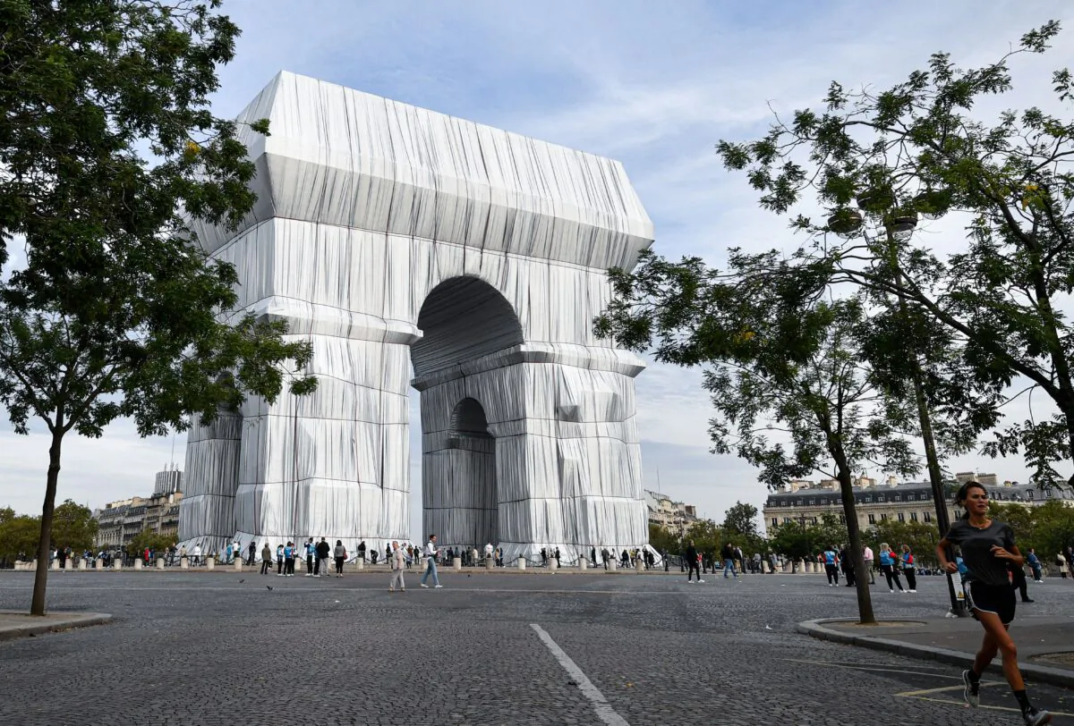 Bystanders walk near the Arc de Triomphe, wrapped in silver-blue fabric, as it was designed by late artist Christo, in Paris as part of the 38th European Heritage Days and the launch of the Cultural Olympiad in Paris, on Sept. 19, 2021. (Alain Jocard/AFP via Getty Images)