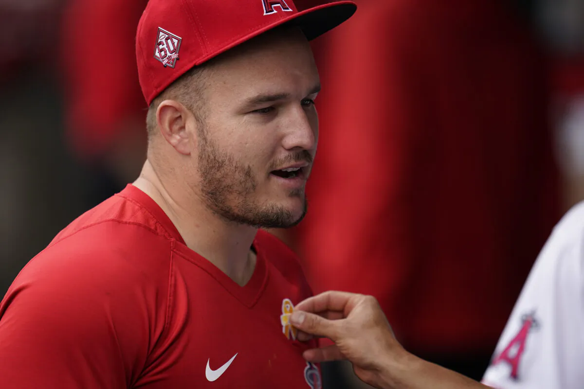 Los Angeles Angels' Mike Trout gets some help to put a yellow ribbon on his shirt in the dugout before a baseball game against the New York Yankees Wednesday, Sep. 1, 2021, in Anaheim, Calif. (Ashley Landis/AP Photo)