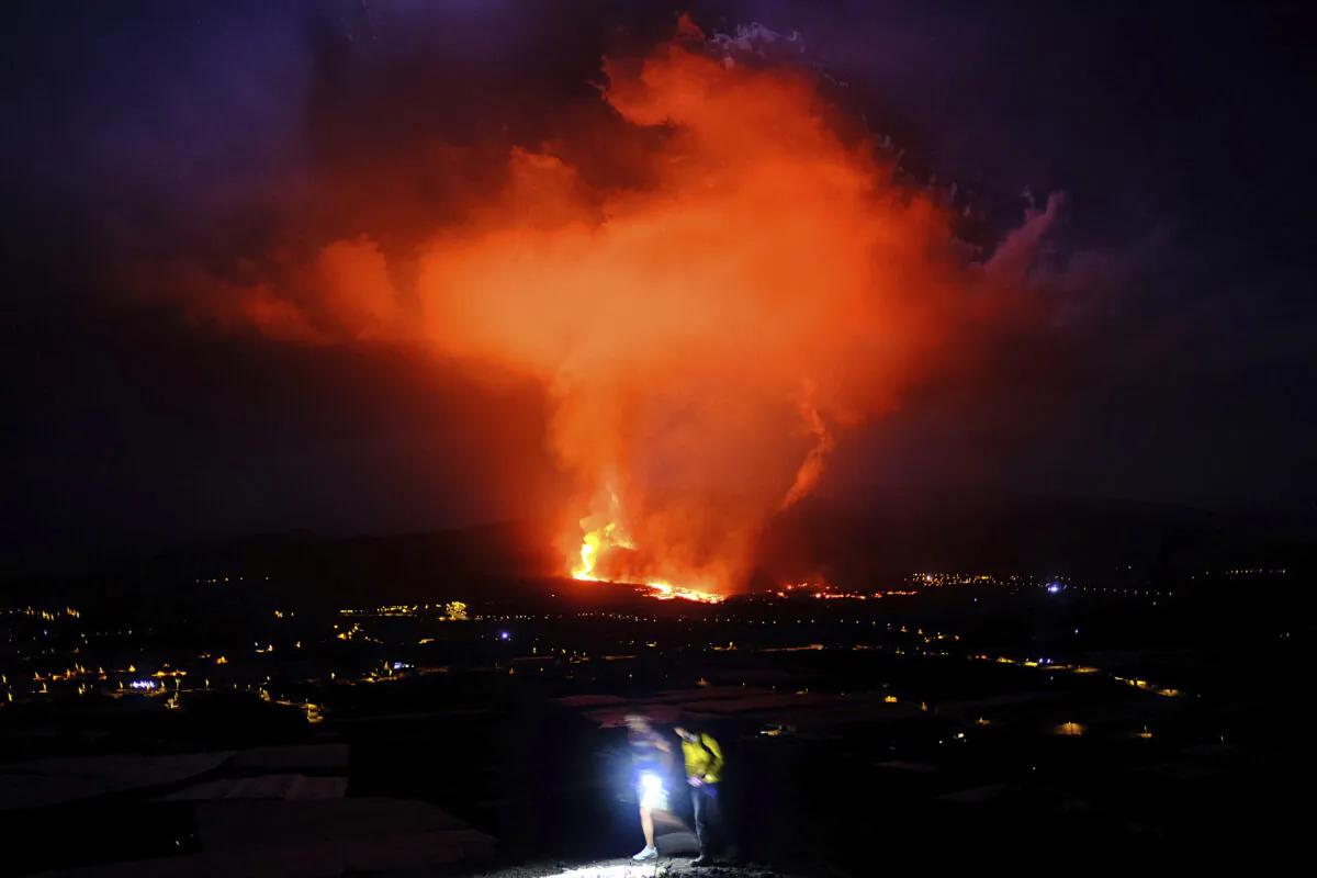 Two people walk as lava spews from a volcano on the Canary island of La Palma, Spain, in the early hours of Sept. 25, 2021. (Daniel Roca /AP Photo)