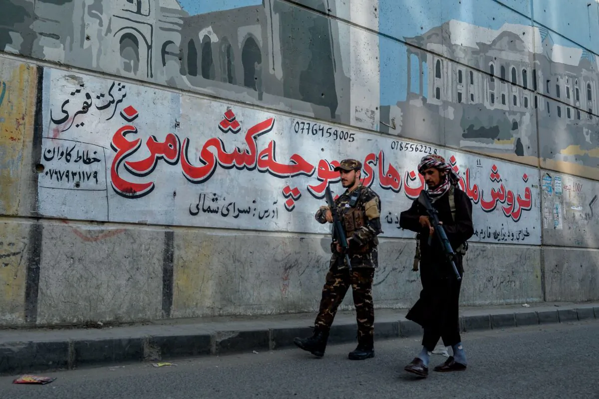 Taliban fighters patrol along a road on the backdrop of a mural pained on the wall of a flyover in Kabul on September 26, 2021. (Hoshang Hashimi/AFP via Getty Images)
