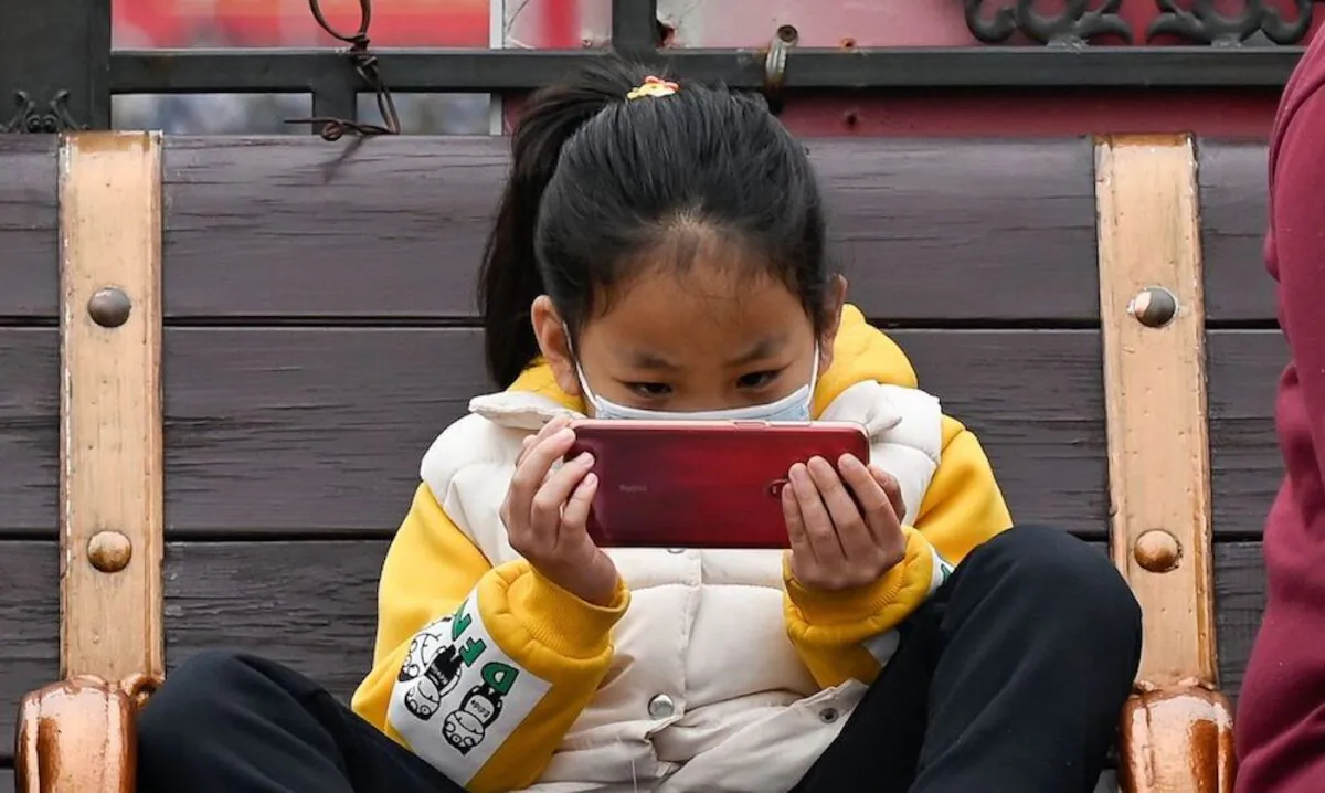 A girl watches a mobile phone as she rests on a bench in Beijing on March 4, 2021. (Wang Zhao/AFP via Getty Images)