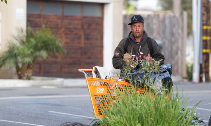 A homeless man stand behind a shopping cart in Oceanside, Calif., on April 14, 2021. (John Fredricks/The Epoch Times)