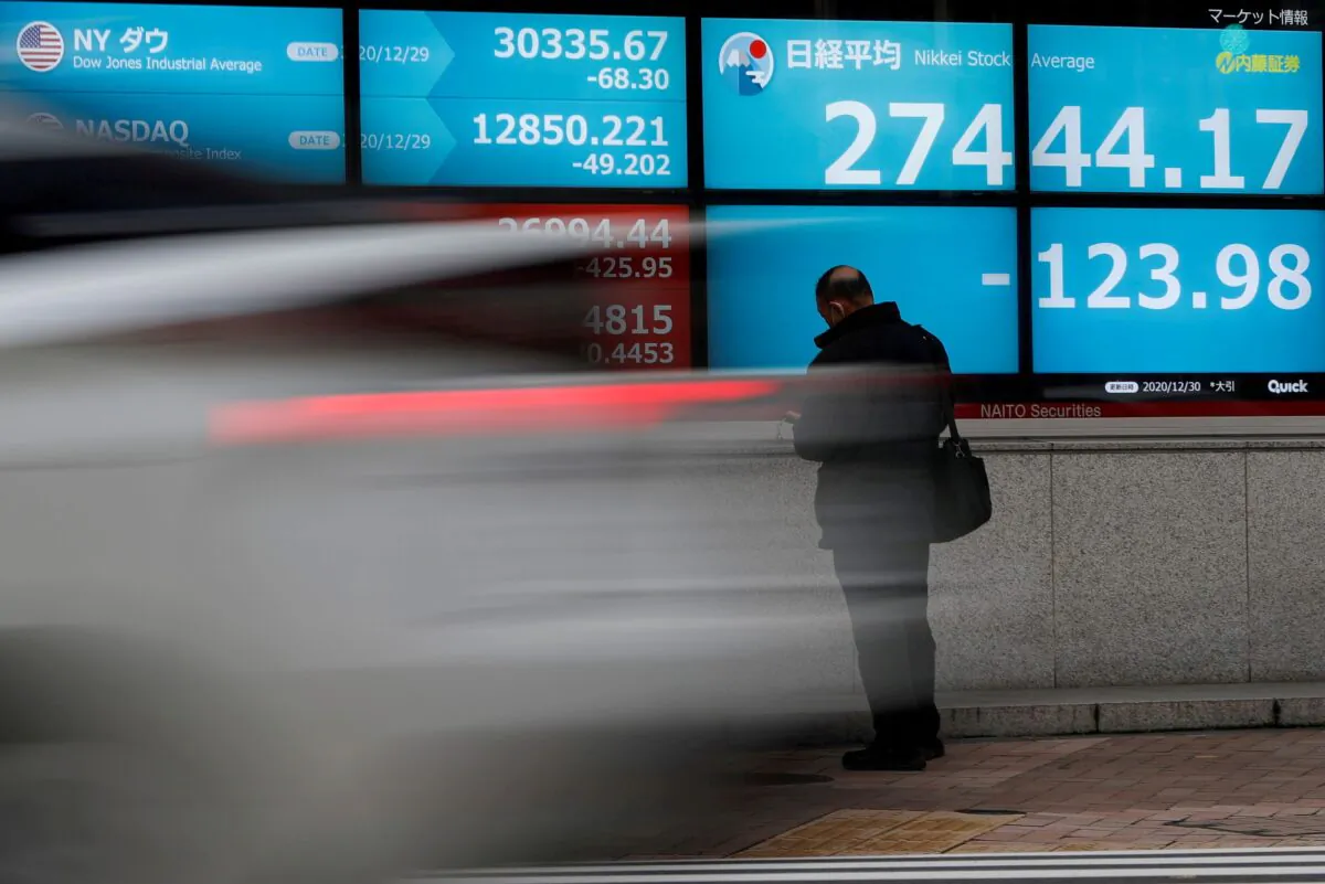 A man stands in front of a screen displaying Nikkei share average and the world's stock indexes outside a brokerage, amid the coronavirus disease (COVID-19) outbreak, in Tokyo, Japan on Dec. 30, 2020. (Issei Kato/Reuters)