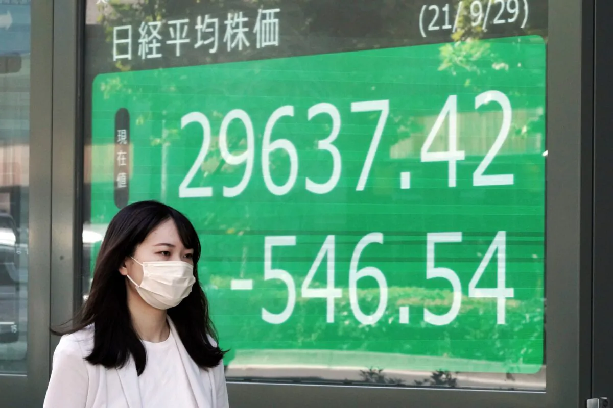 A woman wearing a protective mask walks in front of an electronic stock board showing Japan's Nikkei 225 index at a securities firm in Tokyo, Japan on Sept. 29, 2021. (Eugene Hoshiko/AP Photo)