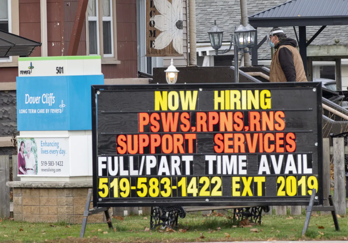 A masked worker walks behind a hiring sign on his way into the Dover Cliffs long term care home in Port Dover, Ont. on Nov. 13, 2020. (The Canadian Press/Frank Gunn)