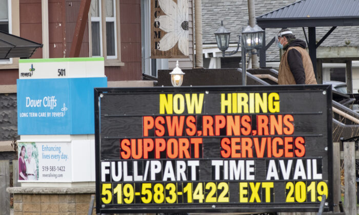 A masked worker walks behind a hiring sign on his way into the Dover Cliffs long term care home in Port Dover, Ont. on Nov. 13, 2020. (The Canadian Press/Frank Gunn)