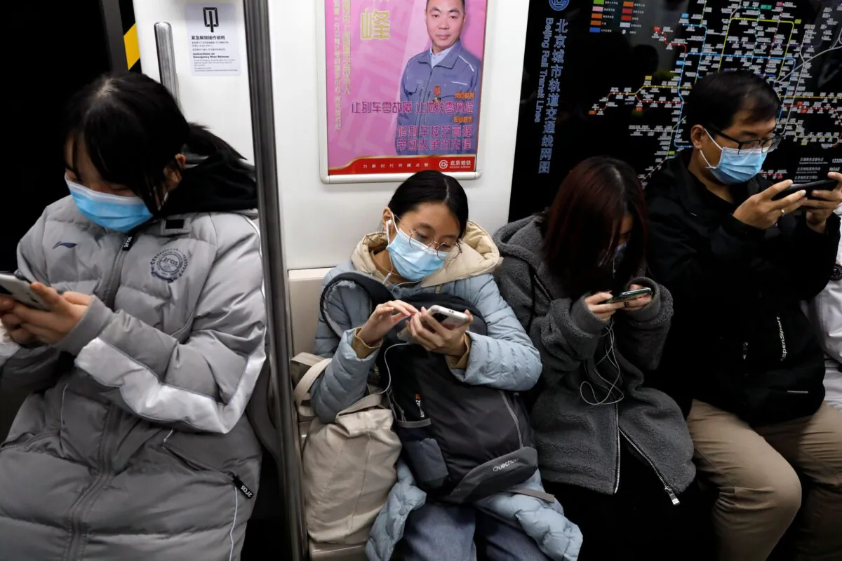 People wearing protective masks look at their mobile phones on a subway train in Beijing, China, on Dec. 25, 2020. (Tingshu Wang/Reuters)