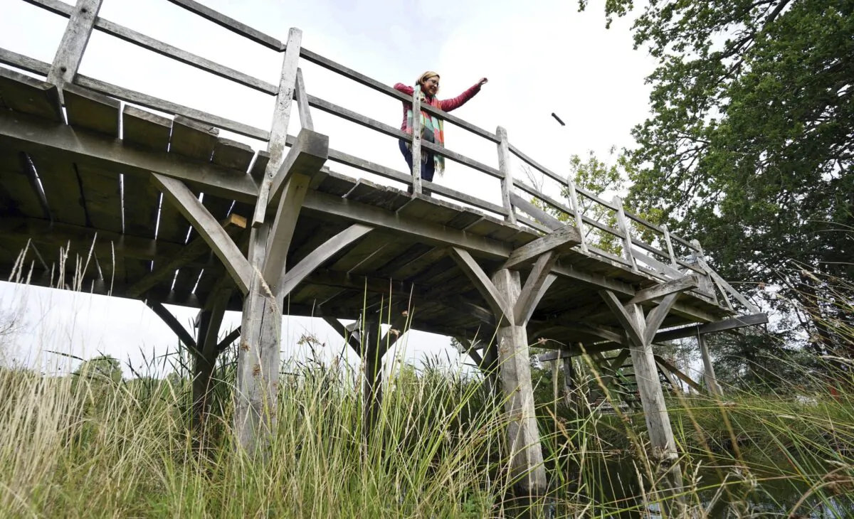 Silke Lohmann of Summers Place Auctions stands on the original Poohsticks Bridge from Ashdown Forest, featured in A.A. Milne's Winnie the Pooh books and E.H. Shepard's illustrations, near its original location in Tonbridge, Kent, England, on Sept. 30, 2021. (Gareth Fuller/PA via AP)