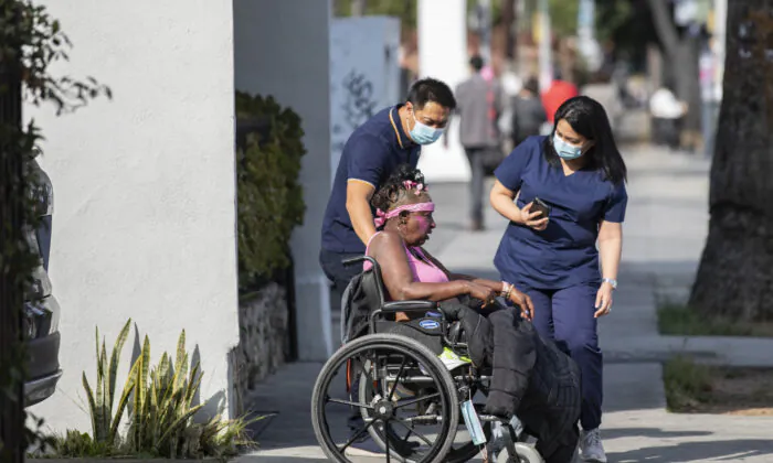 Medical staff assist a disabled homeless woman in front of the Alvarado Care Center in Los Angeles, Calif., on Sept. 29, 2021. (John Fredricks/The Epoch Times)