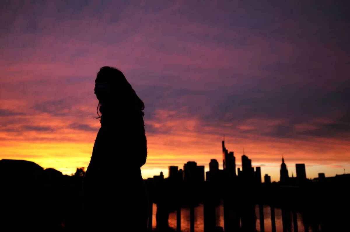  A woman wearing a protective mask walks past the skyline of the financial district during sunset as the spread of the coronavirus disease (COVID-19) continues in Frankfurt, Germany, on Oct. 26, 2020. (Kai Pfaffenbach/Reuters)