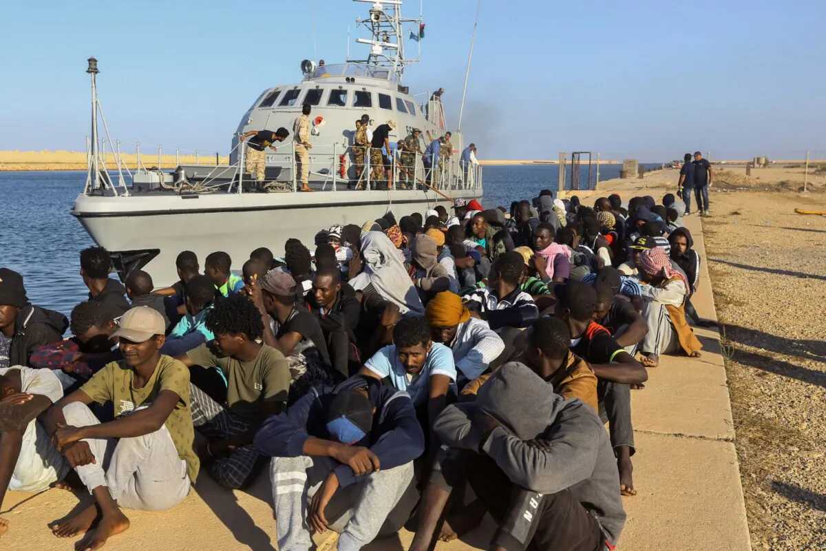 In this photo, rescued migrants looking to use the restive North African country as way to get to Europe, are seated next to a coast guard boat in the city of Khoms, Libya, on Oct. 1, 2019. (Hazem Ahmed/AP Photo)