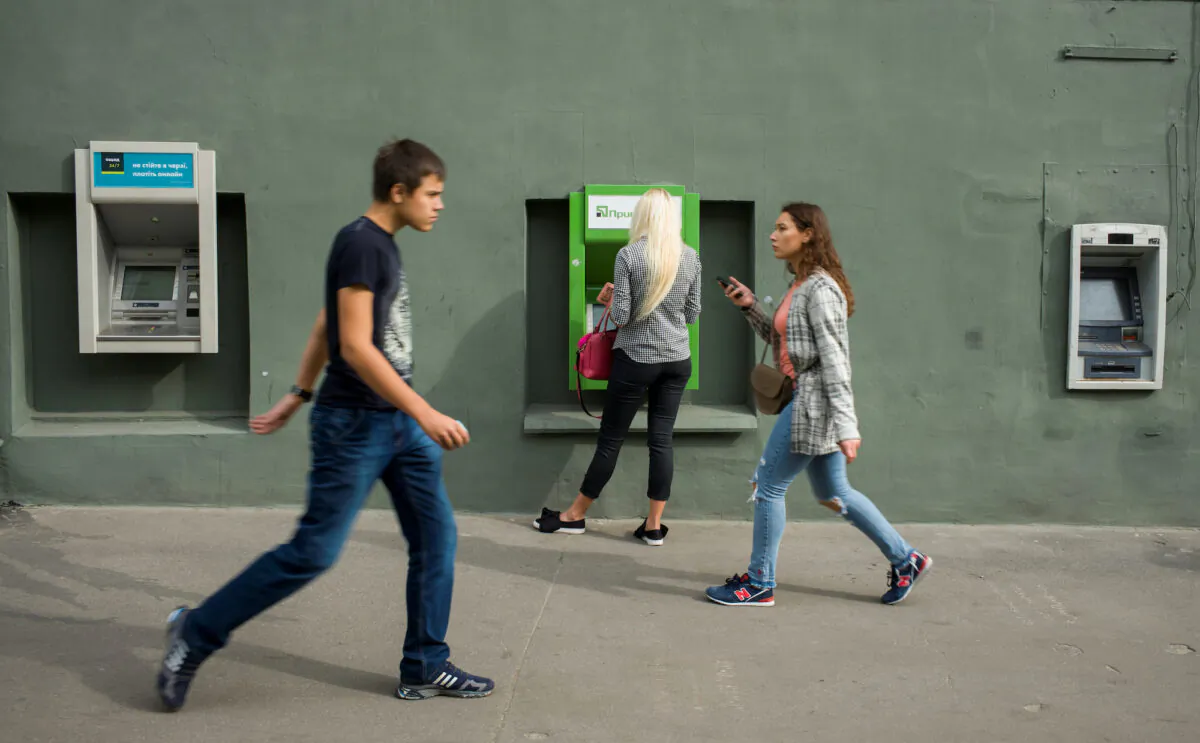 A woman uses an ATM machine as people walk past in central Kharkiv, Ukraine on Sept. 18, 2018. (Gleb Garanich/Reuters)