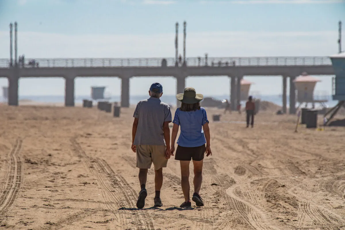 A couple walks along the beach in Huntington Beach, Calif., on Oct. 6, 2021. (John Fredricks/The Epoch Times)