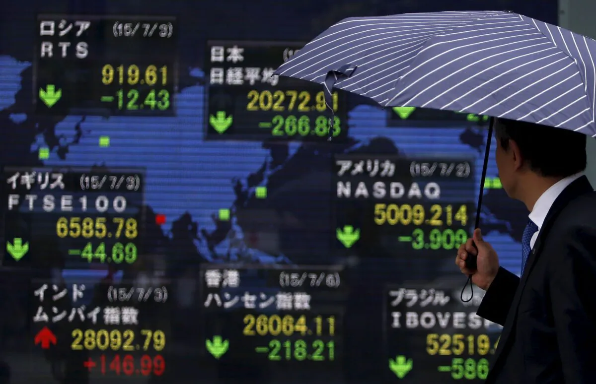 A pedestrian holding an umbrella looks at an electronic board the stock market indices of various countries outside a brokerage in Tokyo, Japan on July 6, 2015. (Yuya Shino/Reuters)