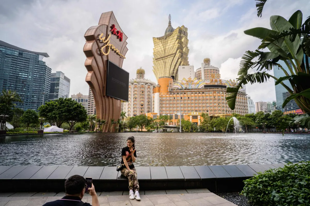 In this photo taken on March 5, 2019, visitors take photos outside the Wynn casino resort with a view of the Grand Lisboa (top C) casino resort building in Macau. (Anthony Wallace/AFP via Getty Images)
