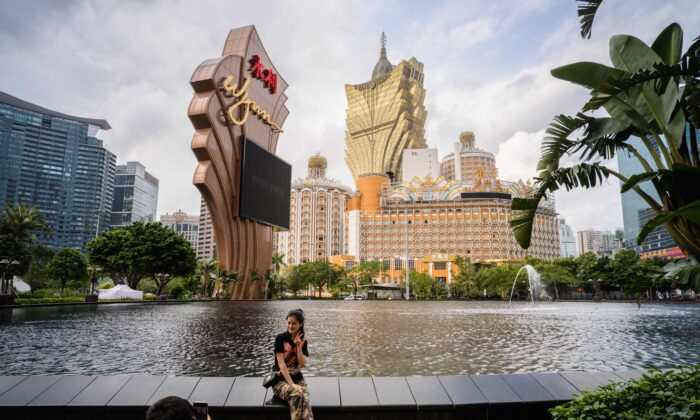 In this photo taken on March 5, 2019, visitors take photos outside the Wynn casino resort with a view of the Grand Lisboa (top C) casino resort building in Macau. (Anthony Wallace/AFP via Getty Images)