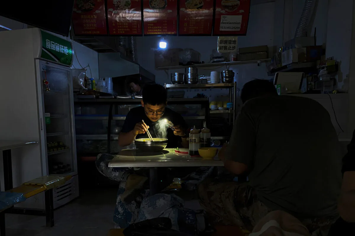 A man uses his smartphone flashlight to light up his bowl of noodles as he eats his breakfast at a restaurant during a blackout in Shenyang, Liaoning Province, China, on Sept. 29, 2021. (Olivia Zhang/AP Photo)