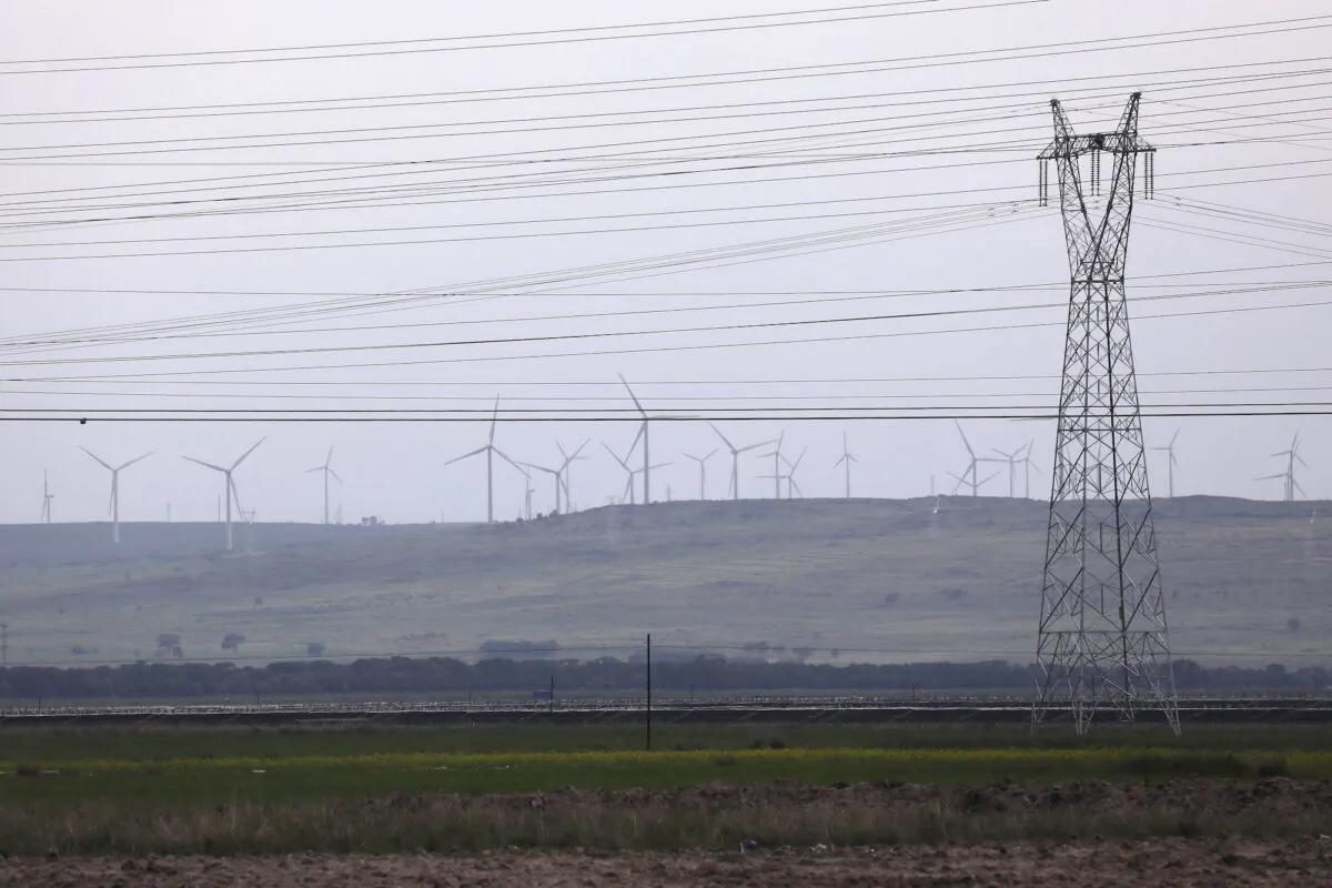An electricity pylon and power lines are seen against a backdrop of wind turbines in Zhangjiakou, Hebei province, China, on July 15, 2021. (Tingshu Wang/Reuters)