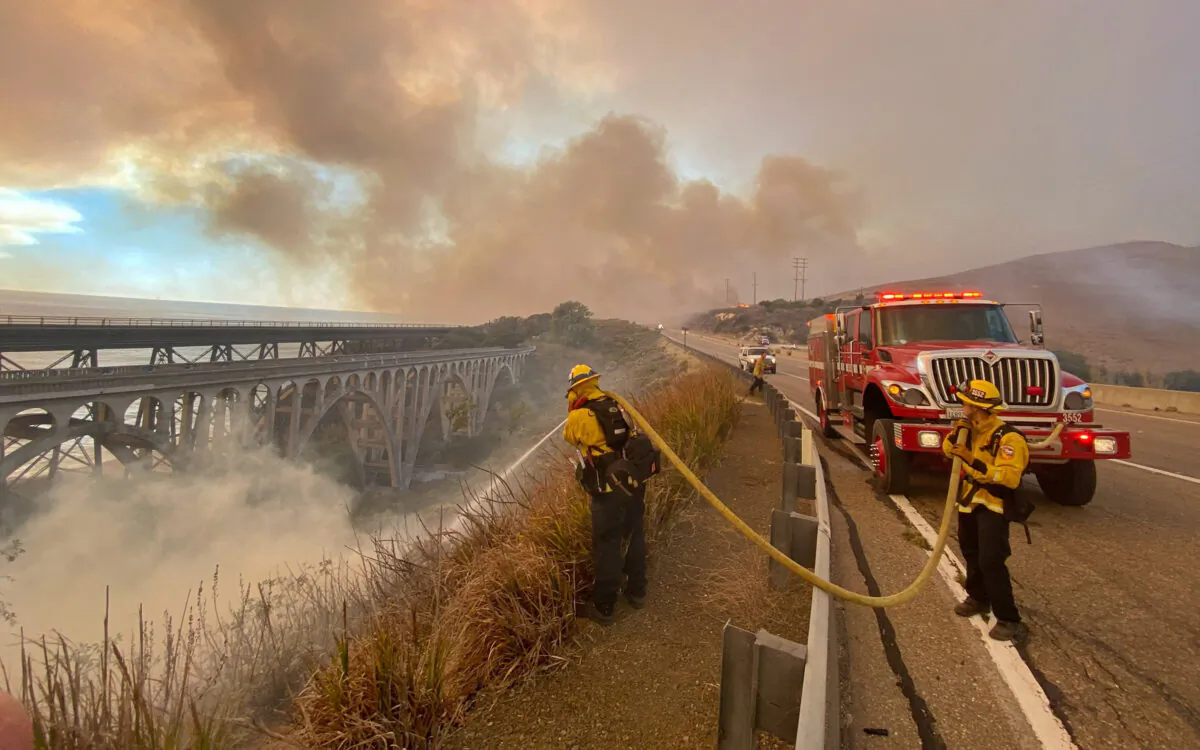 Firefighters extinguish flames that were spotted ahead of the fire front along Highway 101 southbound at Vista Point, north of Refugio State Beach in Santa Barbara County, Calif., on Oct. 12, 2021. (Mike Eliason/Santa Barbara County Fire Department via AP)