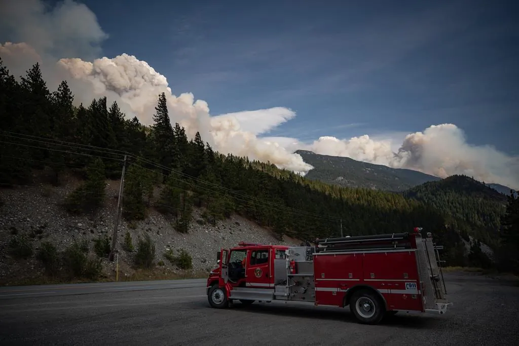 A man sits in a fire truck as the Lytton Creek wildfire burns in the mountains near Lytton, B.C., on August 15, 2021. (The Canadian Press/Darryl Dyck)