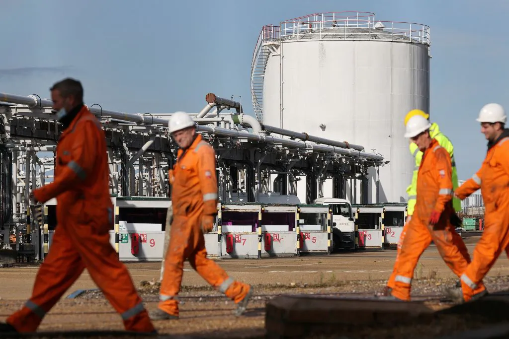 A tanker is stocked with fuel as workers walk past at the Hamble oil refinery near Southampton, England, on Oct. 4, 2021. (Adrian Dennis/AFP via Getty Images)