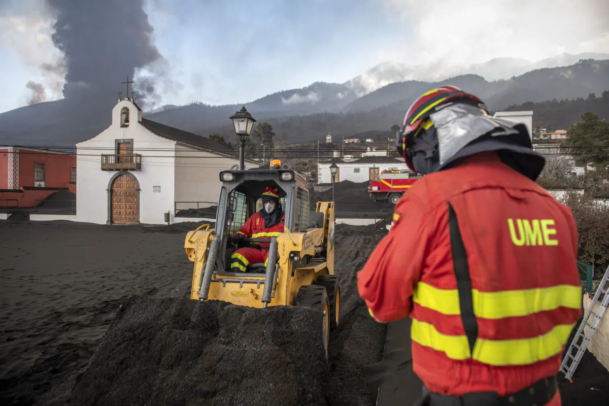 Military Emergency Unit personal clear black ash from volcano as it continues to erupt lava behind a church on the Canary island of La Palma, Spain, on Oct. 13, 2021. (Saul Santos/AP Photo)