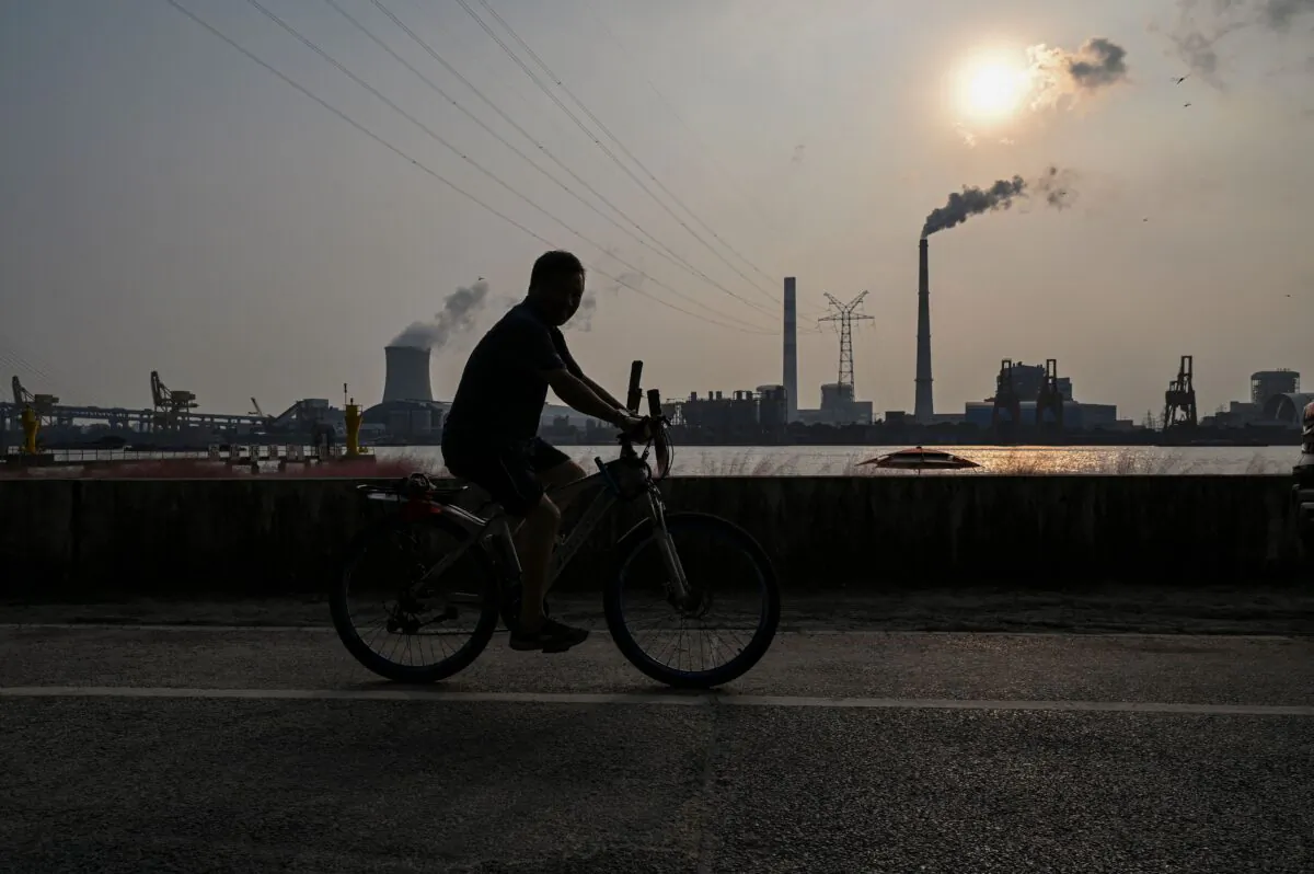 A man rides a bicycle at a promenade along the Huangpu river across the Wujing Coal-Electricity Power Station in Shanghai on Sept. 28, 2021. (Hector Retamal/AFP via Getty Images)