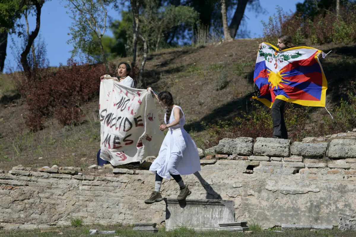 Protesters displaying a Tibetan flag and a banner reading "No genocide games" enter the grounds during the lighting of the Olympic flame at Ancient Olympia site, birthplace of the ancient Olympics, in southwestern Greece, on Oct. 18, 2021. (Thanassis Stavrakis/AP Photo)
