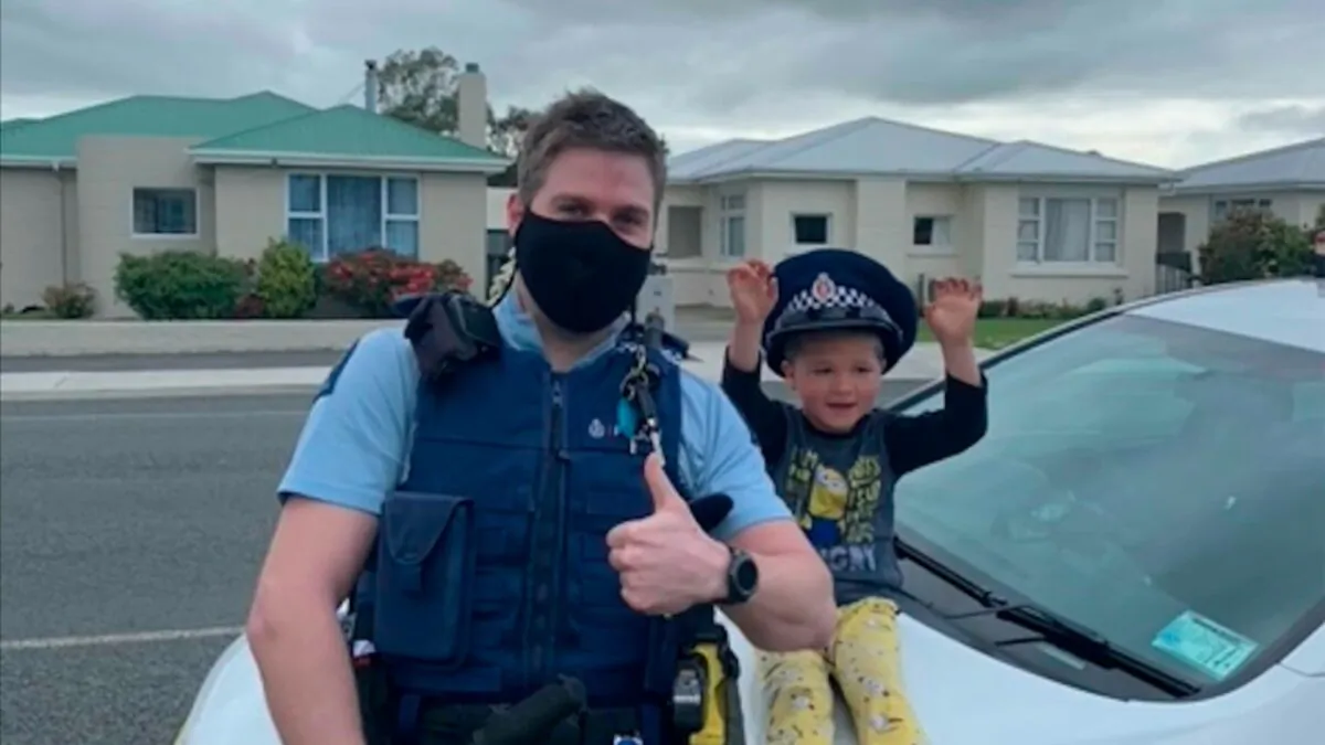 An officer sits on his patrol car with a 4-year-old boy in the South Island city of Invercargill, New Zealand, on Oct. 15, 2021. (NZ Police via AP)