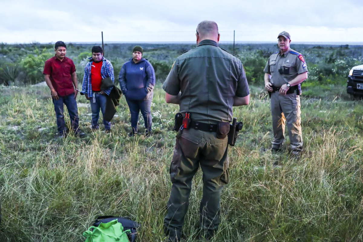 A Border Patrol agent picks up three illegal aliens after Texas state troopers arrested two U.S. citizen smugglers who were transporting them to San Antonio, in Kinney County, Texas, on Oct. 20, 2021. (Charlotte Cuthbertson/The Epoch Times)