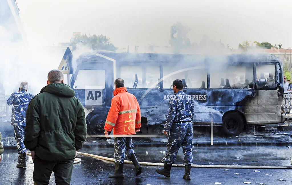 In this photo released by the Syrian official news agency SANA, Syrian firefighters and security officer check a burned bus at the site of a deadly explosion, in Damascus, Syria, Wednesday, Oct. 20, 2021. Two roadside bombs exploded near a bus carrying troops during the morning rush hour in the Syrian capital early Wednesday, killing and wounding several people, state TV reported. (SANA via AP)