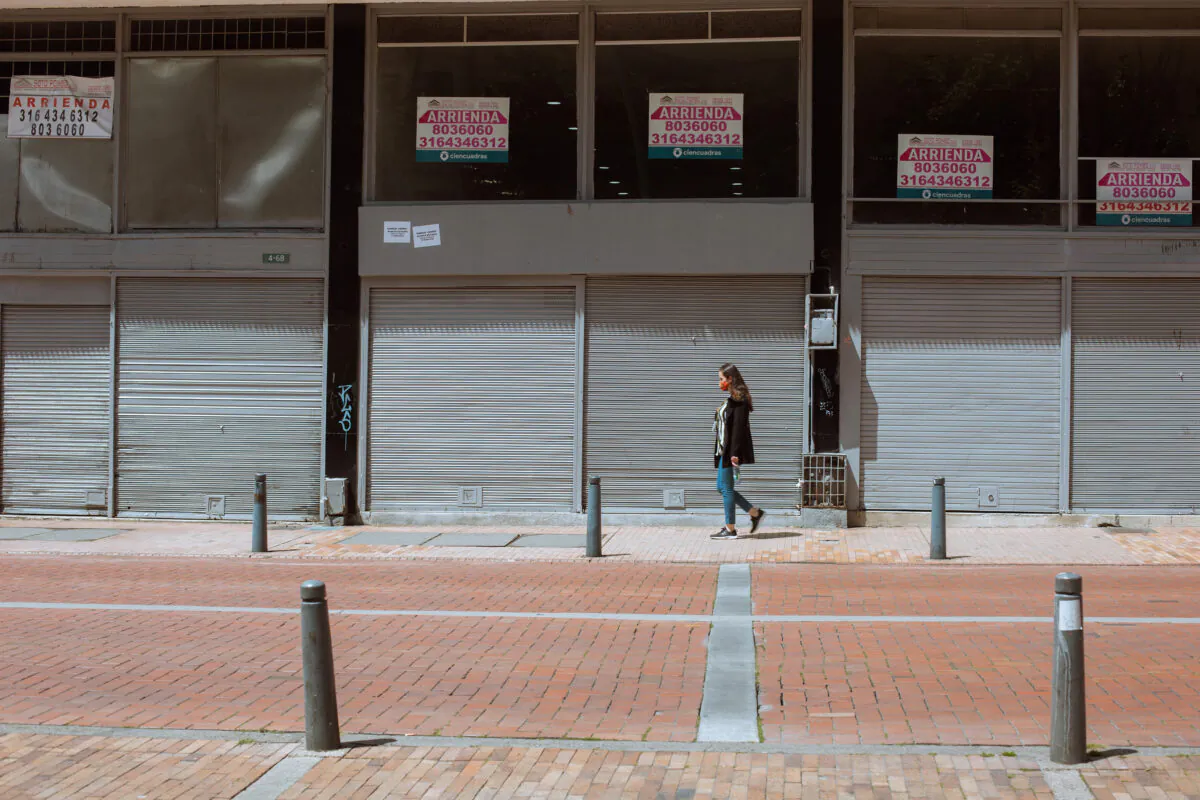 A pedestrian walks by empty business windows featuring rental signs in Bogotá, Colombia, on Oct. 15, 2021. (Alejandro Gomez/The Epoch Times)