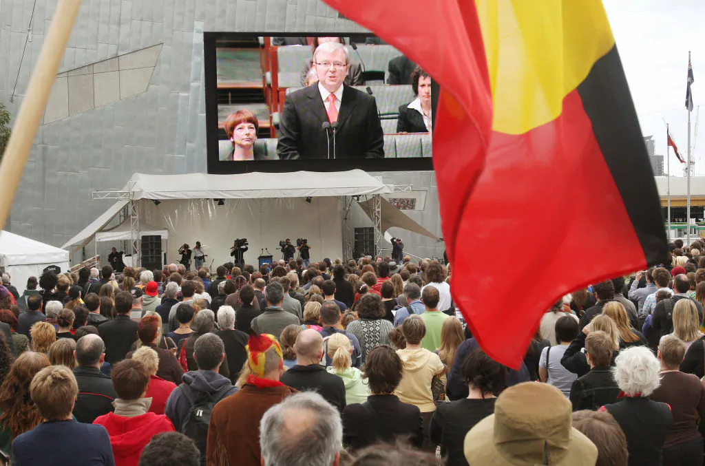 An Aboriginal flag waves in front of the giant television screen as thousands gather in Melbourne's Federation Square, Australia, on Feb. 13, 2008 to listen to Prime Minister Kevin Rudd deliver an historic apology in parliament to the Aboriginal people for injustices committed over two centuries of white settlement. (William West/AFP via Getty Images)