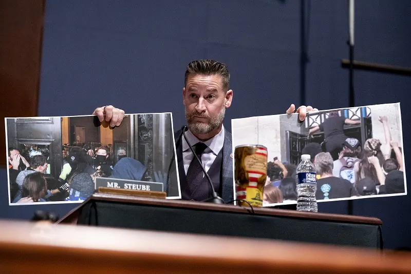 Rep. Greg Steube (R-Fla.) holds a photo from the Jan. 6 attack on the Capitol (L) and the Oct. 14 protest at the Interior Department (R) as he questions U.S. Attorney General Merrick Garland at a House Judiciary Committee hearing at the U.S. Capitol in Washington on Oct. 21, 2021. (Greg Nash-Pool/Getty Images)