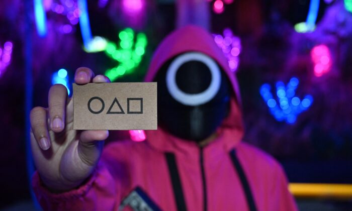 A waiter dressed in an outfit from the Netflix series "Squid Game" holds a card while playing a game to attract customers at a cafe in Jakarta on Oct. 19, 2021. (Adek Berry/AFP via Getty Images)