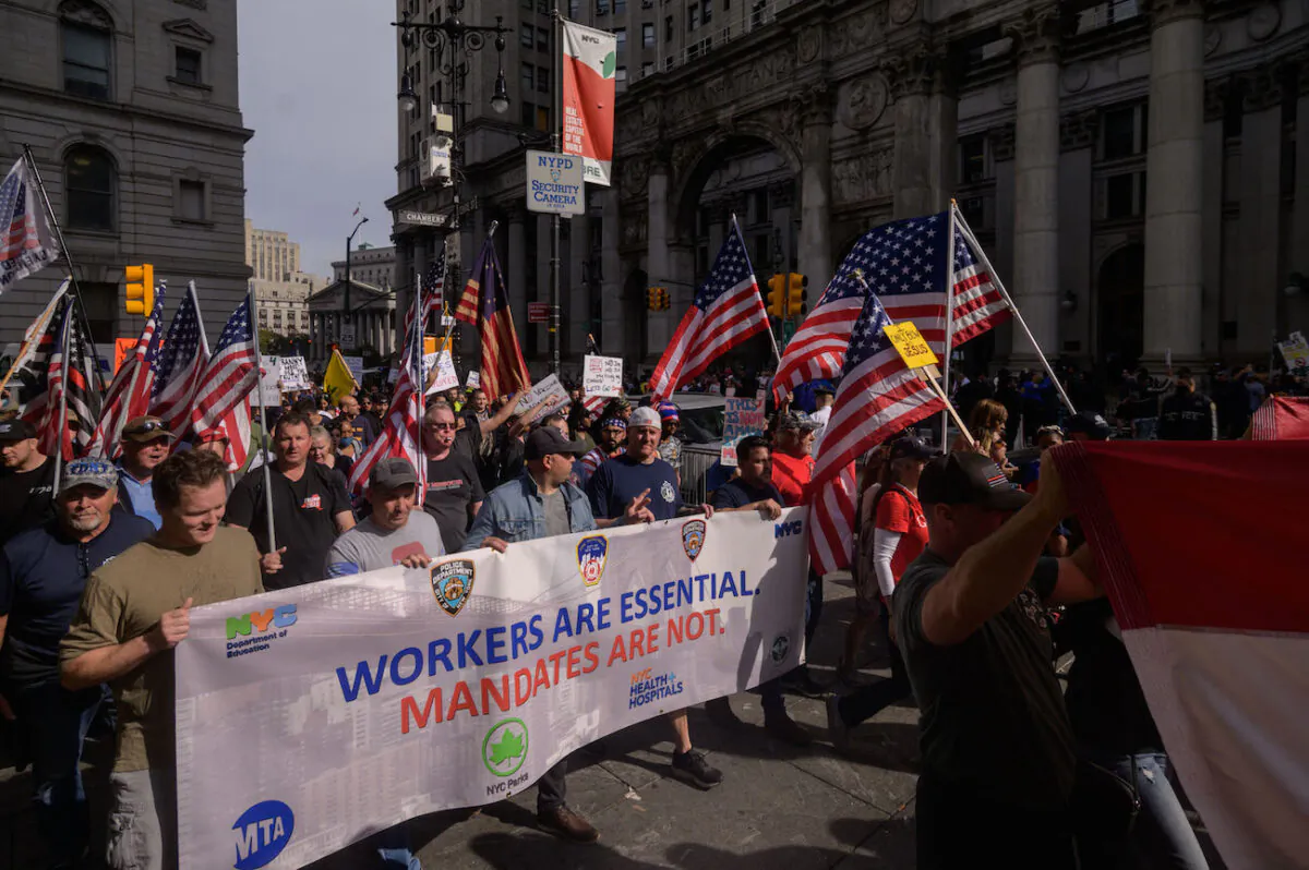 Municipal workers hold placards and shout slogans as they march across Brooklyn bridge during a protest against the COVID-19 vaccine mandate, in New York, on Oct. 25, 2021. (Ed Jones/AFP via Getty Images)