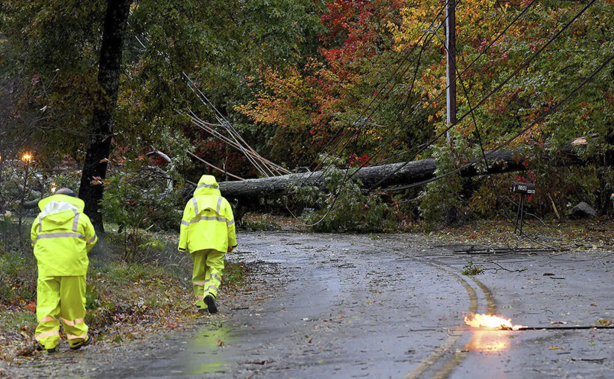 Crew members of the North Attleboro Electric Dept. survey the damage done by a toppled tree that took down utility lines as a primary line arcs on Reservoir Street in North Attleboro, Mass., on Oct. 27, 2021. (Mark Stockwell/The Sun Chronicle via AP)