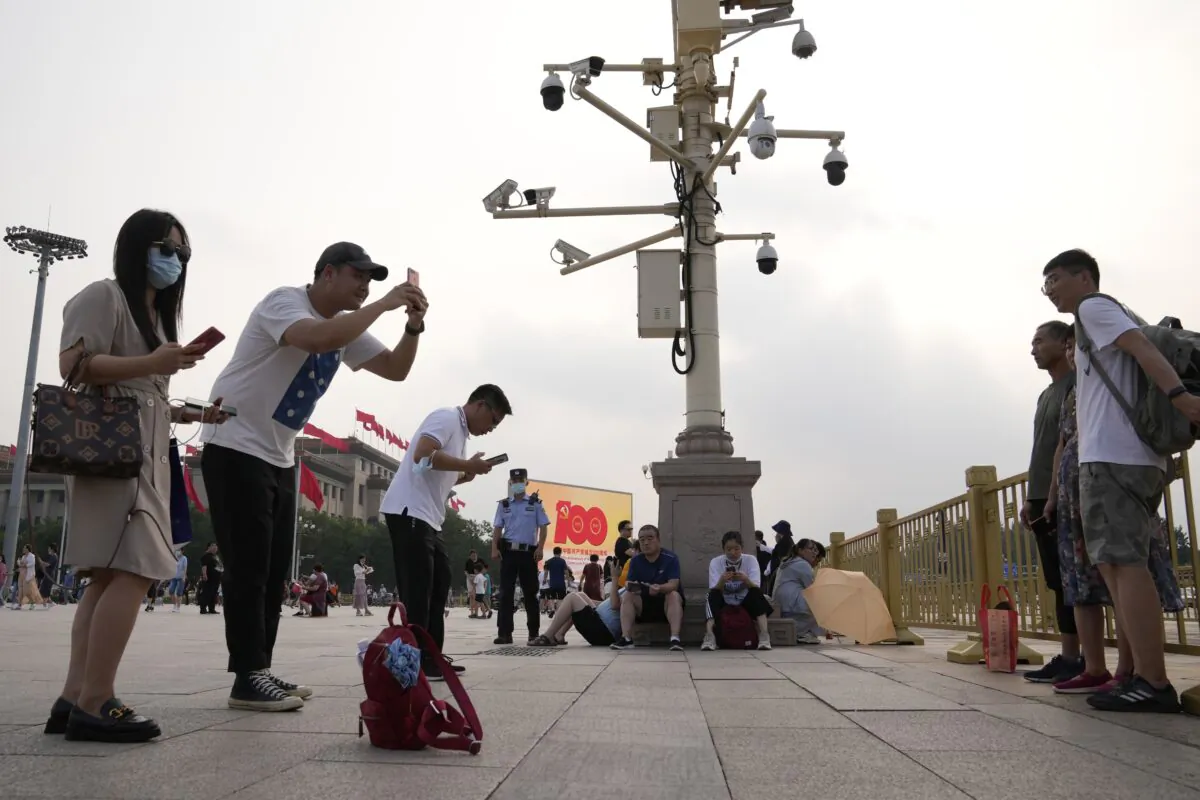 Visitors take photos near surveillance cameras as a policeman stand watch nearby on Tiananmen Square in Beijing on July 15, 2021. (Ng Han Guan/AP Photo)