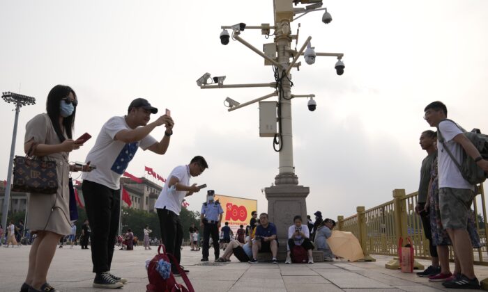 Visitors take photos near surveillance cameras as a policeman stand watch nearby on Tiananmen Square in Beijing on July 15, 2021. (Ng Han Guan/AP Photo)