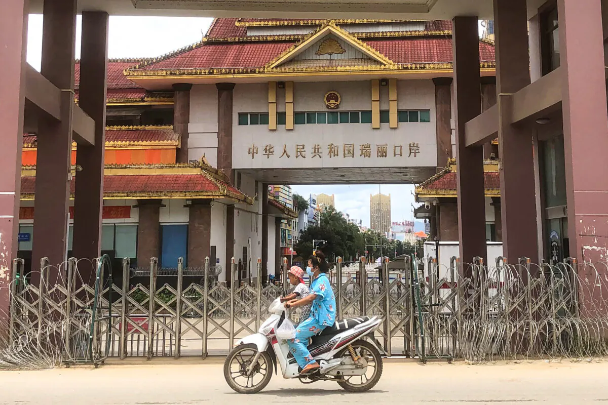 A woman and child ride a scooter past the China-Myanmar border gate in Muse, Burma on July 5, 2021. (STR/AFP via Getty Images)